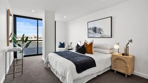 A modern bedroom with a large bed, a side table, a desk with a plant, and a window with a city view. - Hobart CBD Roof Top Penthouse (Hobart)