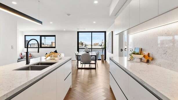 A modern kitchen with a central island, a dining area with a table and chairs, and a large window providing a view of the city. - Hobart CBD Roof Top Penthouse (Hobart)