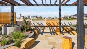 An outdoor patio with a pergola, stone planters, and wooden stools. - Hobart CBD Roof Top Penthouse (Hobart)