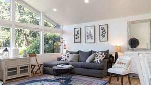 A cozy living room with a grey sofa, a patterned rug, and a large window with a view of greenery.