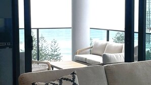 A balcony with a white sofa and a patterned pillow, overlooking a snowy landscape and a body of water. - Boardwalk Burleigh Beach 1 bed (Burleigh Heads)