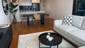 A modern living room with a sofa, a coffee table, and a dining area with chairs and a table. - Boardwalk Burleigh Beach 1 bed (Burleigh Heads)