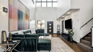 Un salon spacieux avec un canapé d’angle, une table basse et un grand tableau abstrait accroché au mur.