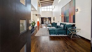 Un vaste espace de vie doté d’un haut plafond, d’un grand tableau abstrait et d’un ensemble de meubles de salon modernes.
