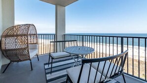 Un balcó amb vista a la platja, que inclou una cadira de vimet, una taula rodona i una cadira de metall negre.