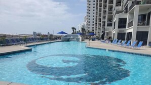 Una piscina amb disseny en espiral, envoltada de gandules i un edifici de grans alçades al fons.