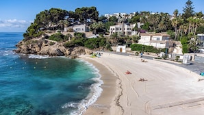 Una playa costera con aguas turquesas cristalinas, una orilla arenosa y una colina con edificios residenciales.
