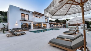 Una casa moderna de dos pisos con piscina, mobiliario exterior y una pérgola.