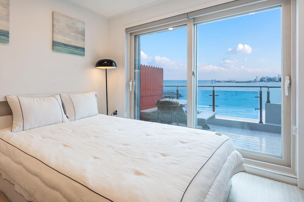 A bedroom with a large bed, a sliding glass door to a balcony, and a view of the sea.