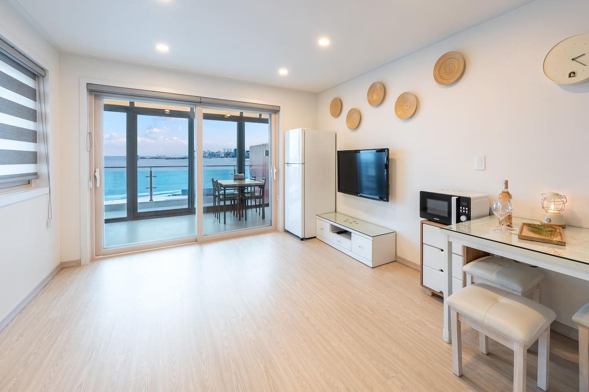 A modern living room with a large TV, a microwave, and a dining area with a table and chairs.