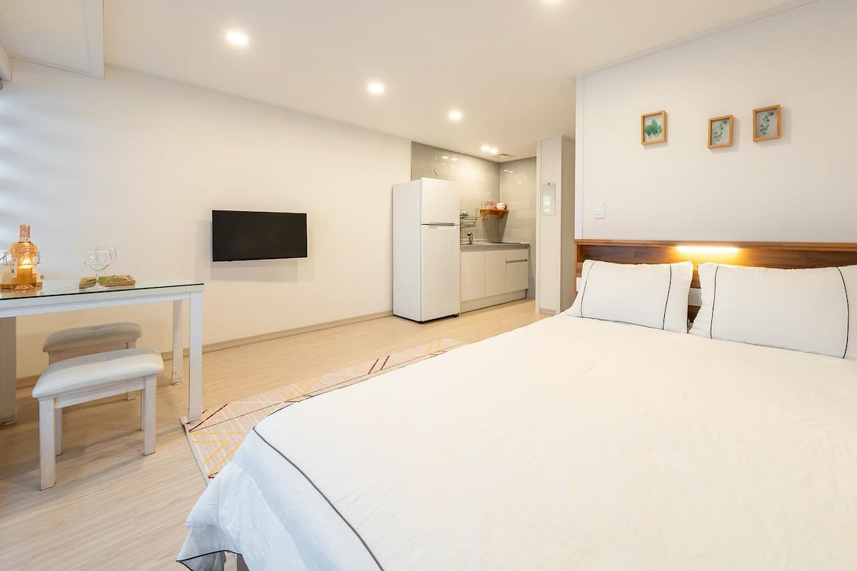 A hotel room with a bed, a desk with a chair, a television, a refrigerator, and a small kitchen area.
