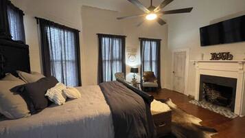 A bedroom with a bed, a ceiling fan, a fireplace, and a television mounted above it.