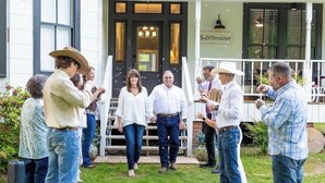 Un grupo de personas de pie frente a un edificio con porche y un letrero que dice 'Bed & Breakfast'.