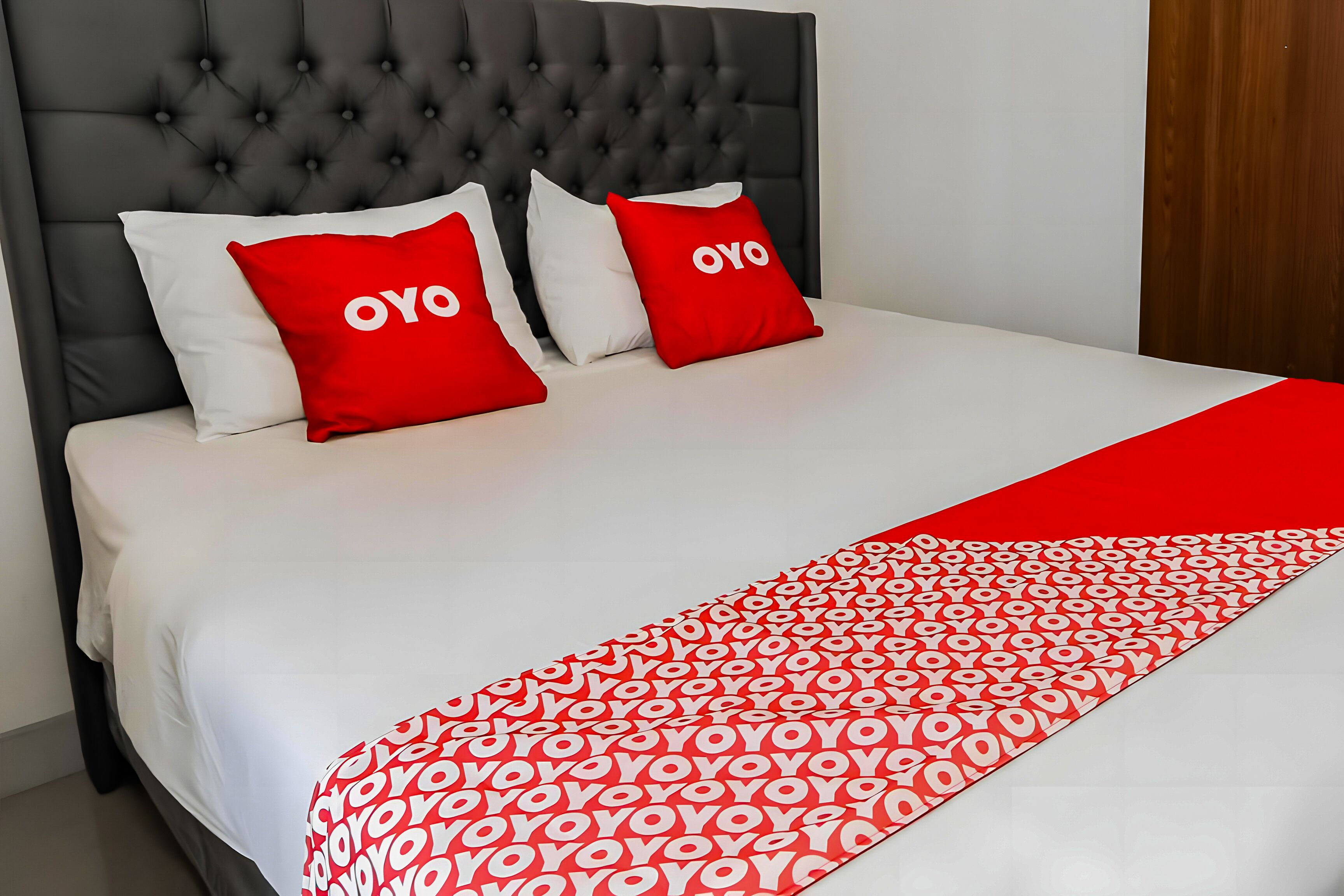 Un letto con copripiumino bianco e rosso, due cuscini rossi con la scritta "OYO" e una testiera imbottita.