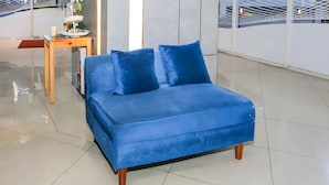 A blue sofa bed with wooden legs, a small wooden table with a cup and decorative item, and a white tiled floor. - Collection O Fortune 88 Kamala Lagoon Reception at Indomaret and White Forest (Bekasi)