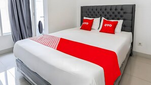 A neatly made bed with a white and red bedspread, two red pillows with the word "OYO" on them, and a grey upholstered headboard. - Collection O Fortune 88 Kamala Lagoon Reception at Indomaret and White Forest (Bekasi)
