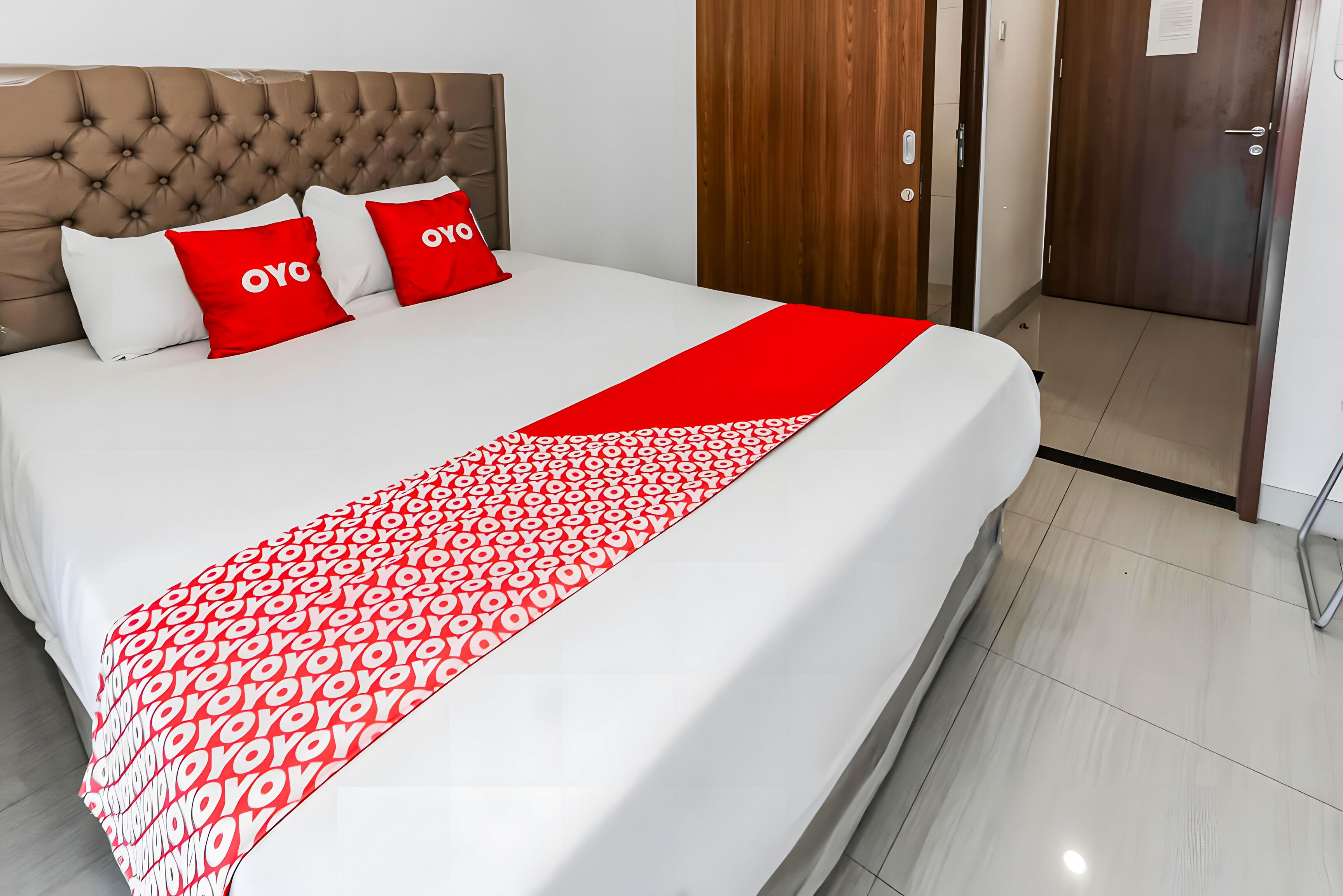 A hotel room with a bed, a red and white patterned bedspread, and two red pillows with the word "OYO" on them.