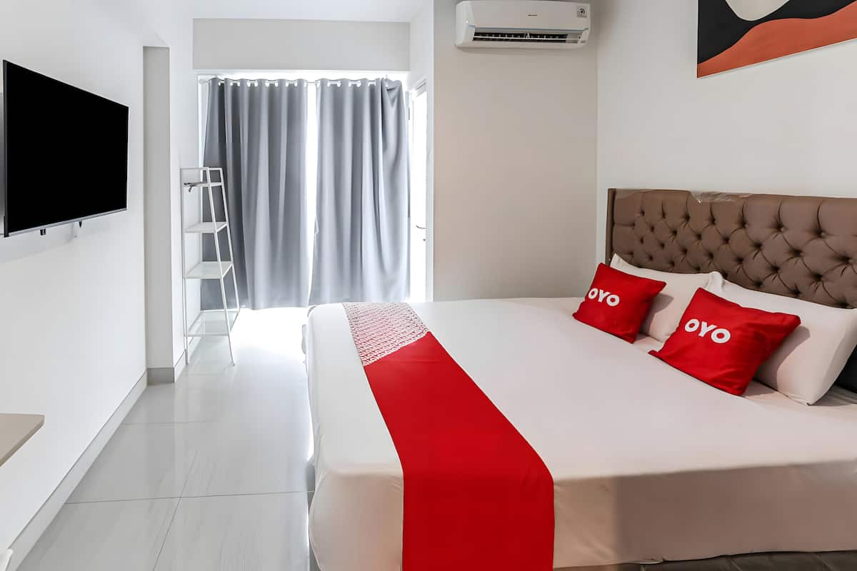 A modern hotel room with a large bed, a flat-screen TV mounted on the wall, a window with curtains, and an air conditioning unit.