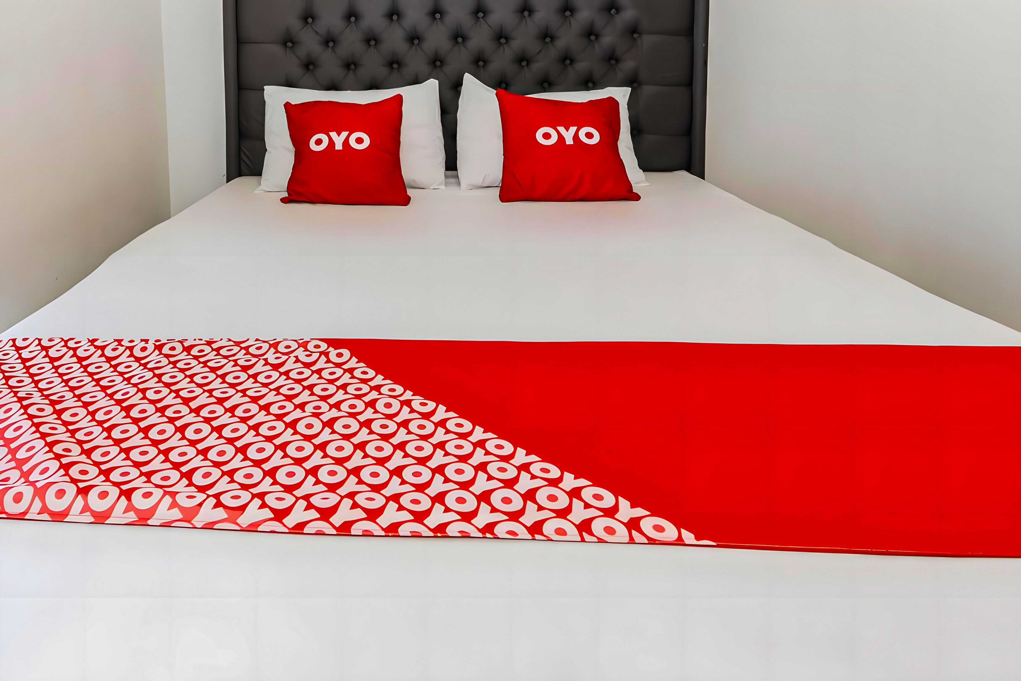 A bed with a white and red bedspread, two red pillows with "OYO" text, and a tufted headboard.