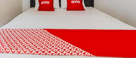 A bed with a white and red bedspread, two red pillows with "OYO" text, and a tufted headboard.