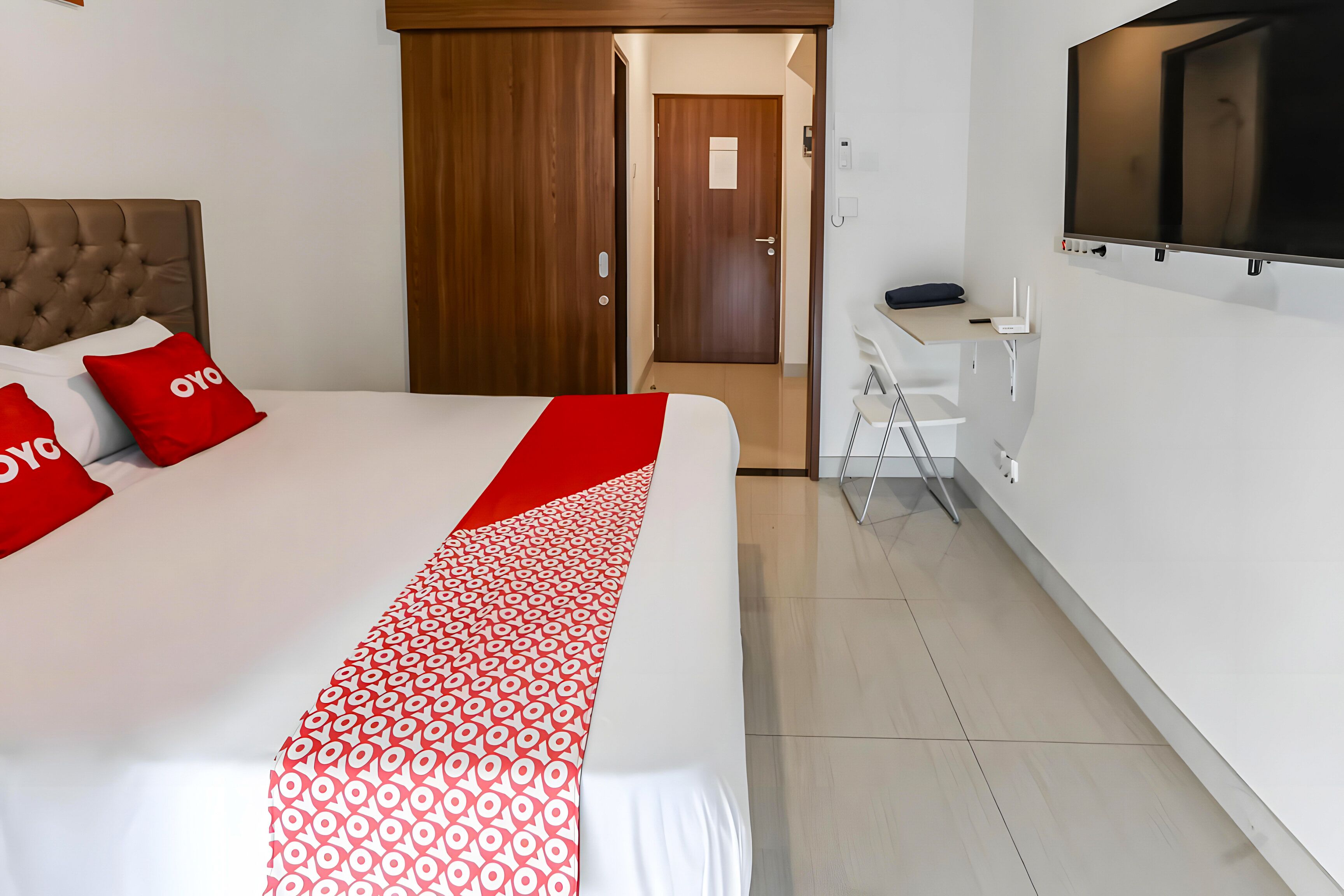 A hotel room with a large bed, a TV mounted on the wall, and a desk with a chair.