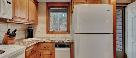 A compact kitchen with wooden cabinets, a built-in microwave, a refrigerator, and a dishwasher.