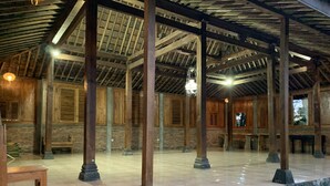 Une vaste salle dotée de poutres en bois apparentes et de piliers en pierre, avec un plancher ciré et un banc.