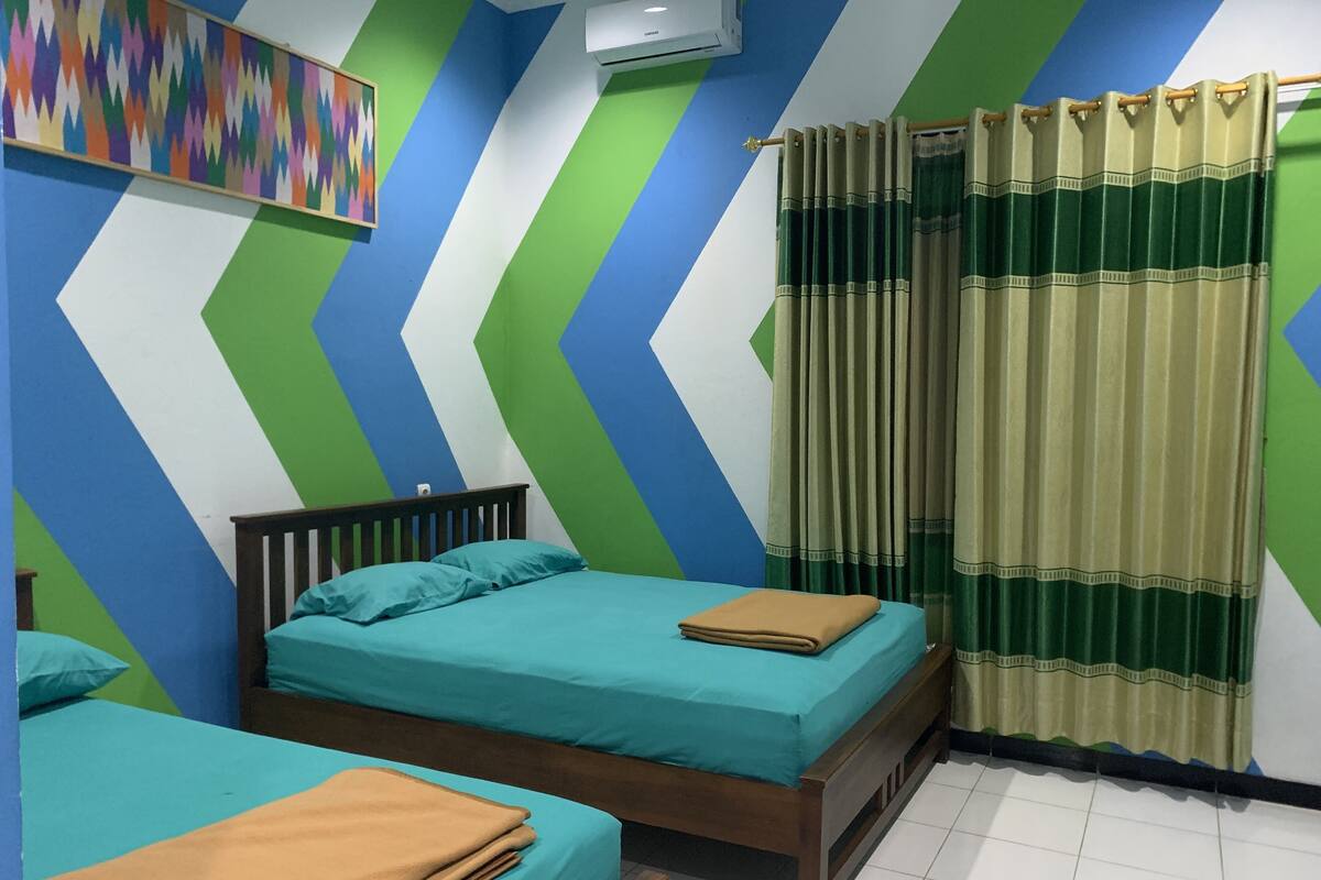Una habitación con dos camas, un diseño de pared colorido y una cortina.