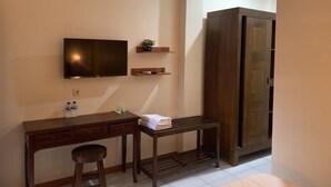 Une chambre d’hôtel avec un bureau en bois, un téléviseur fixé au mur, une armoire et une petite table avec un banc.