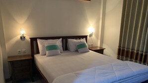 Un lit bien fait, avec une literie blanche et deux oreillers, une tête de lit en bois, des tables de chevet avec des lampes et une fenêtre avec des stores.