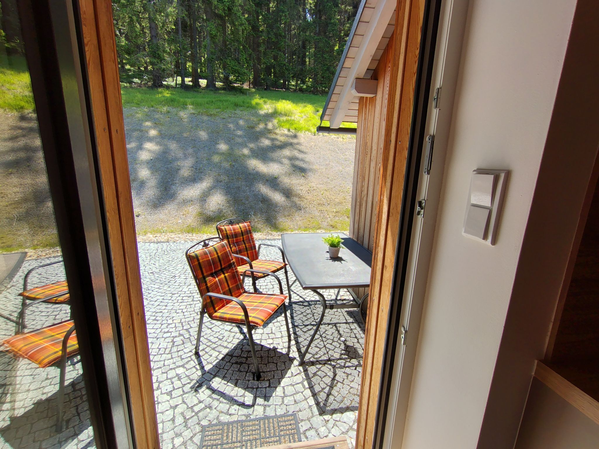 Eine Terrasse mit Tisch und Stühlen, einem kleinen Blumentopf und Blick auf ein bewaldetes Gebiet.