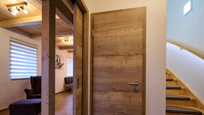 A wooden door with a metal handle, a staircase with wooden steps, and a room with a chair and a table. - Pod lesem by Interhome (Smržovka)