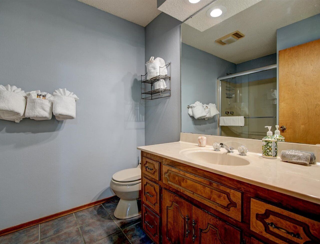 A bathroom with a beige sink, wooden vanity, and a mirror. There are towels hanging on the wall and a shower visible in the background.