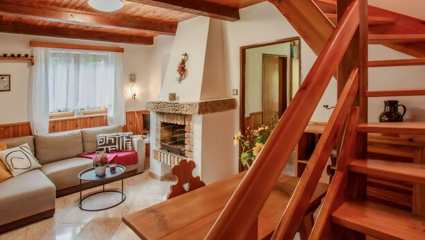A cozy living room with a fireplace, wooden staircase, and a sofa. - Žabovřesky by Interhome (Dehtáře)