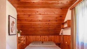 A bedroom with a wooden ceiling, a bed with a gray patterned bedspread, a nightstand, a dresser, and a framed picture on the wall. - Žabovřesky by Interhome (Dehtáře)