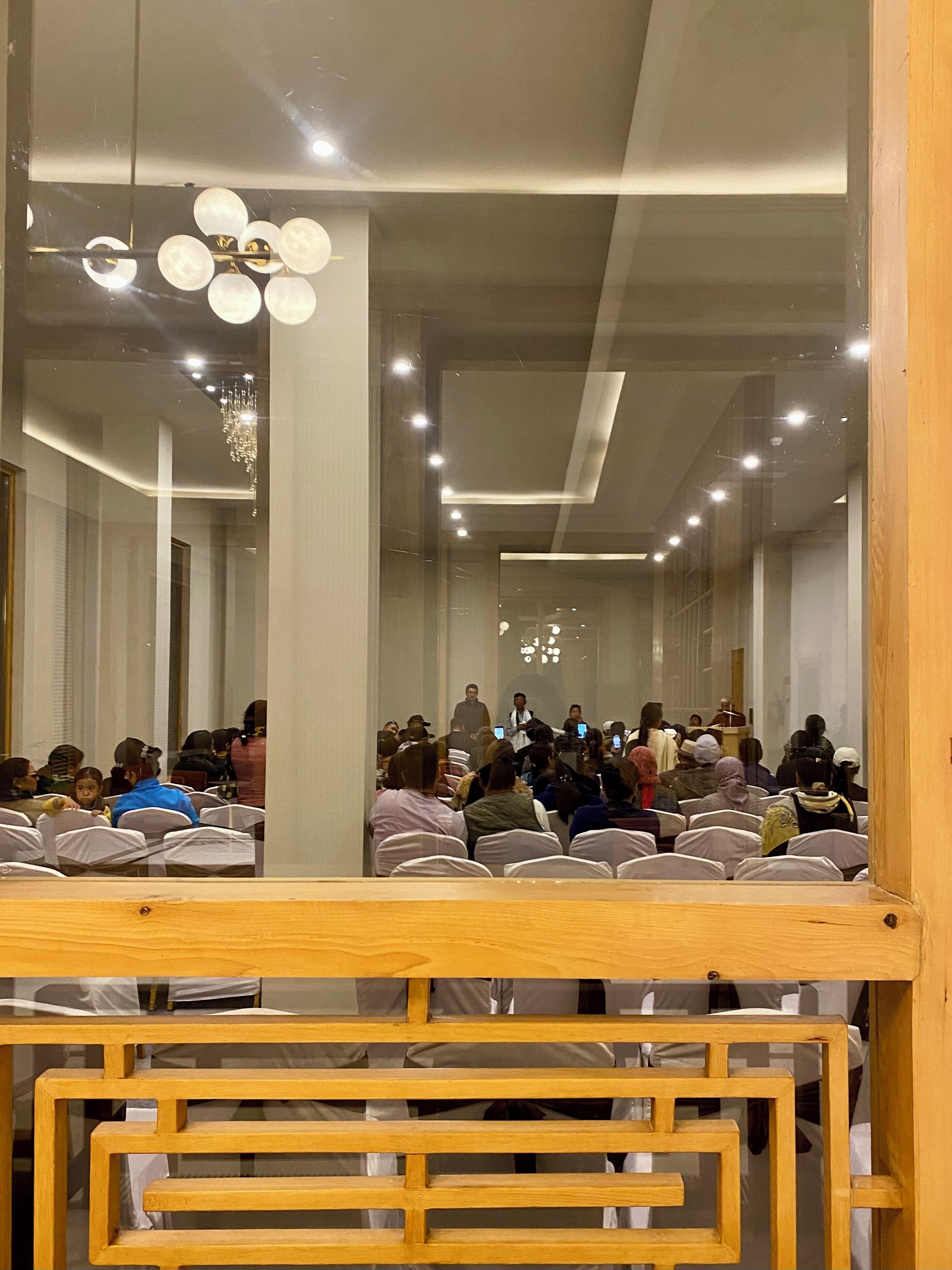 A conference room with rows of white chairs, a wooden podium, and a chandelier.