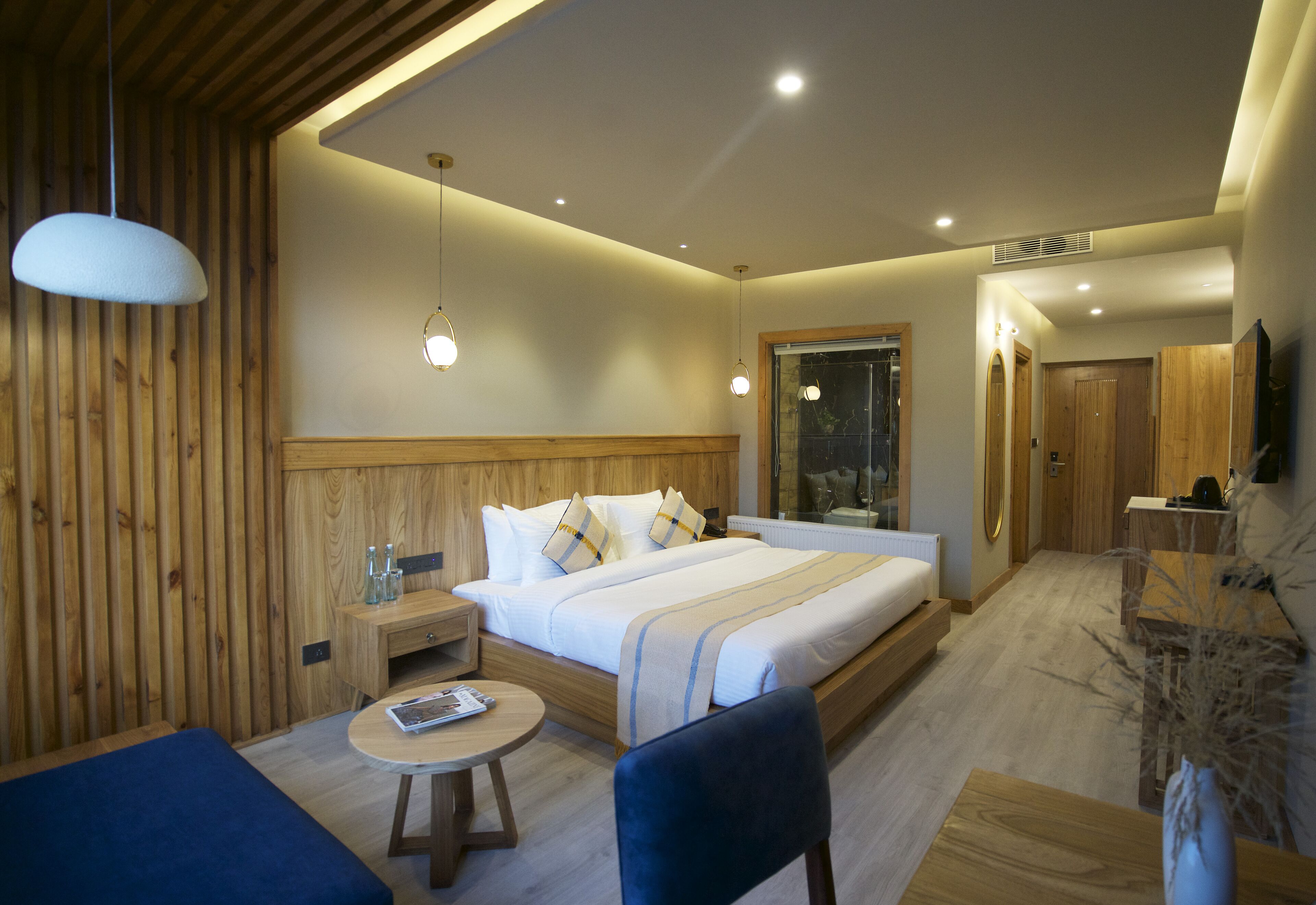 A modern hotel room with a large bed, bedside tables, a round table, and a seating area.