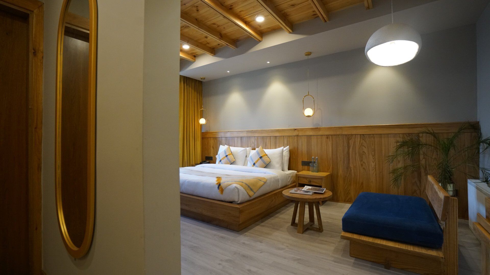 A bedroom with a wooden headboard, a bed with white linens, a bedside table with a lamp, and a blue bench.