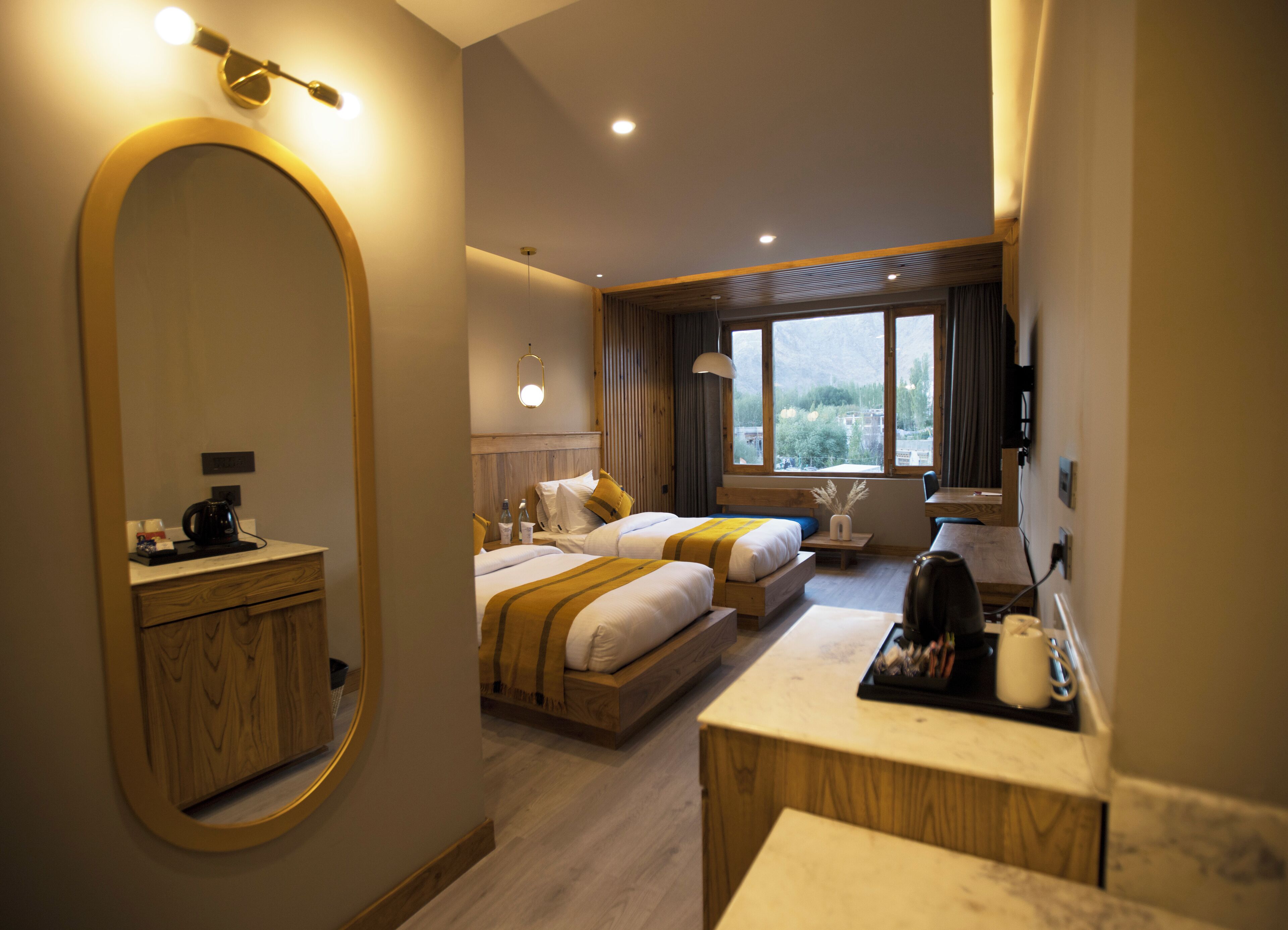 Habitación de hotel con dos camas, un escritorio de madera, un espejo grande y vista a las montañas por la ventana.