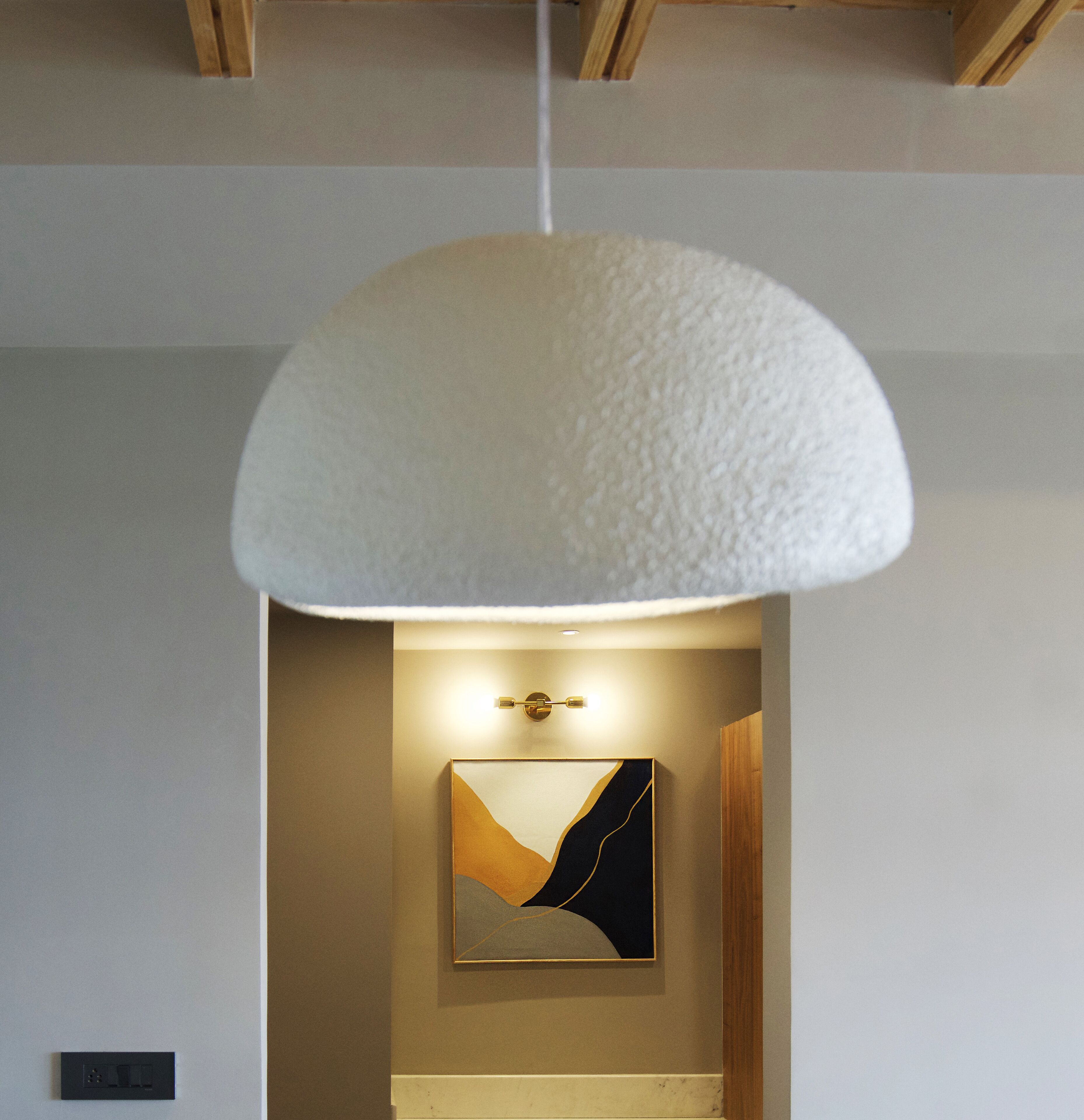 A modern interior with a white textured pendant light, a framed abstract painting, and a wooden ceiling structure.