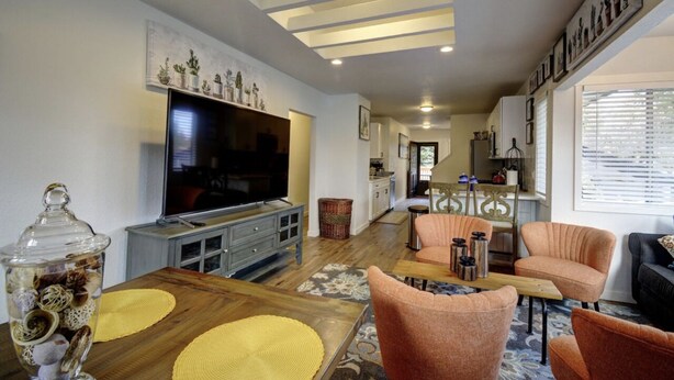 A living room with a TV, wooden coffee table, orange chairs, and a kitchen in the background. - Bright & Airy 4 Bedroom Villa in North Tacoma (Tacoma)