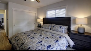 A bedroom with a bed, a ceiling fan, a window with blinds, a nightstand with a lamp, and a door. - Bright & Airy 4 Bedroom Villa in North Tacoma (Tacoma)
