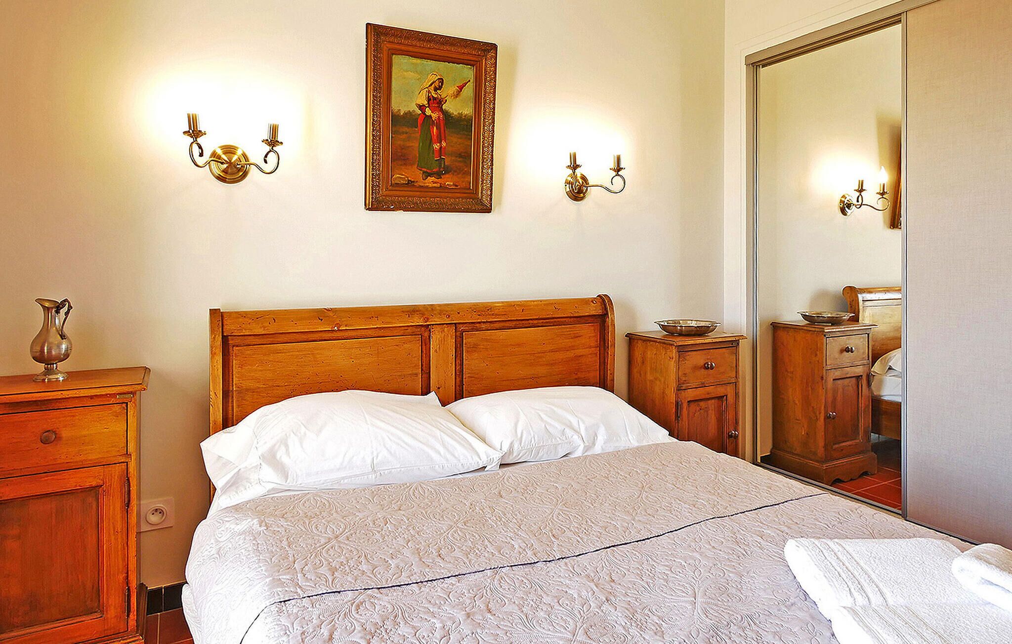 Ein Schlafzimmer mit einem hölzernen Kopfende, zwei Nachttischen, einem großen Spiegel und einem Gemälde an der Wand.