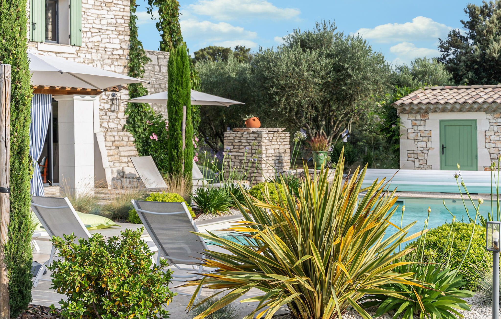 Un espace aménagé au bord de la piscine, avec des chaises longues, un mur en pierre et une vue sur la piscine.
