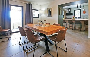 Un coin repas avec une table en bois et six chaises, une cuisine à l’arrière-plan et une vue à travers une porte vitrée.