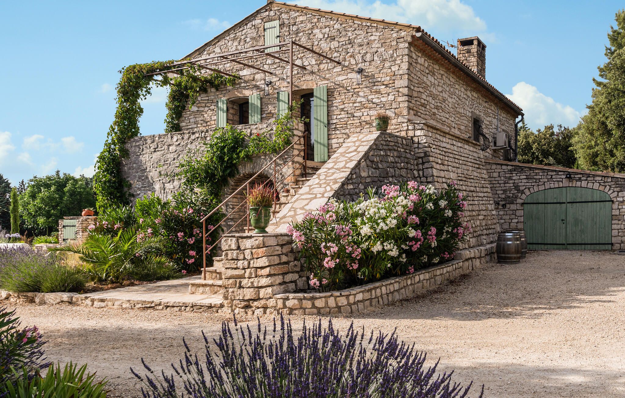 A stone building with a staircase, a green door, and a garden with lavender and pink flowers.