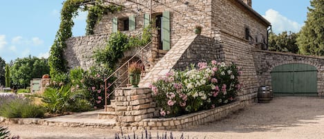 En byggnad av sten med en trappa, en grön dörr och en trädgård med lavendel och rosa blommor.