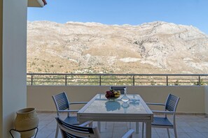 A balcony with a table and chairs, a vase, and a view of a mountainous landscape.