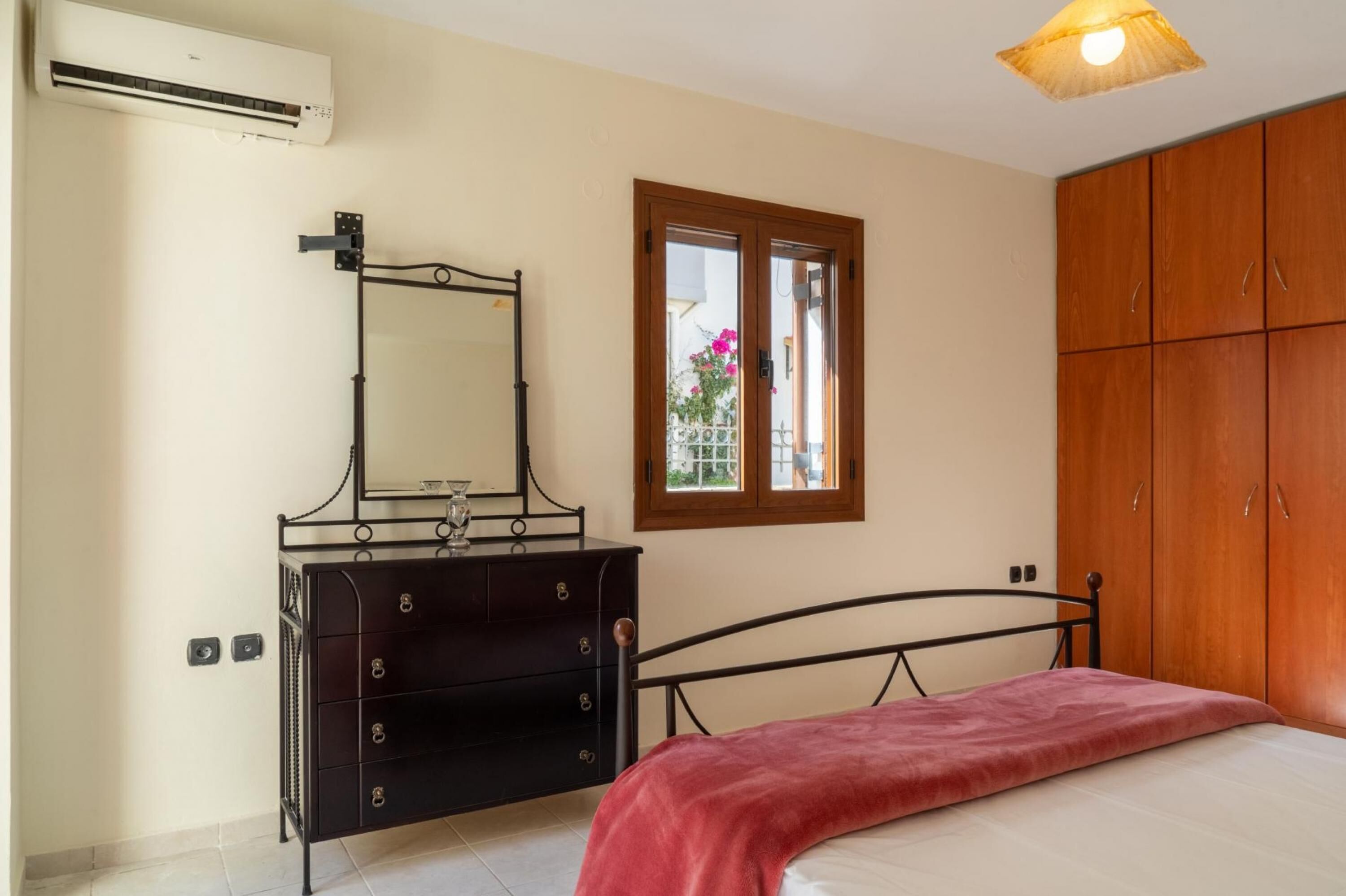 A bedroom with a bed, a dresser, a window with a view, and a wardrobe.