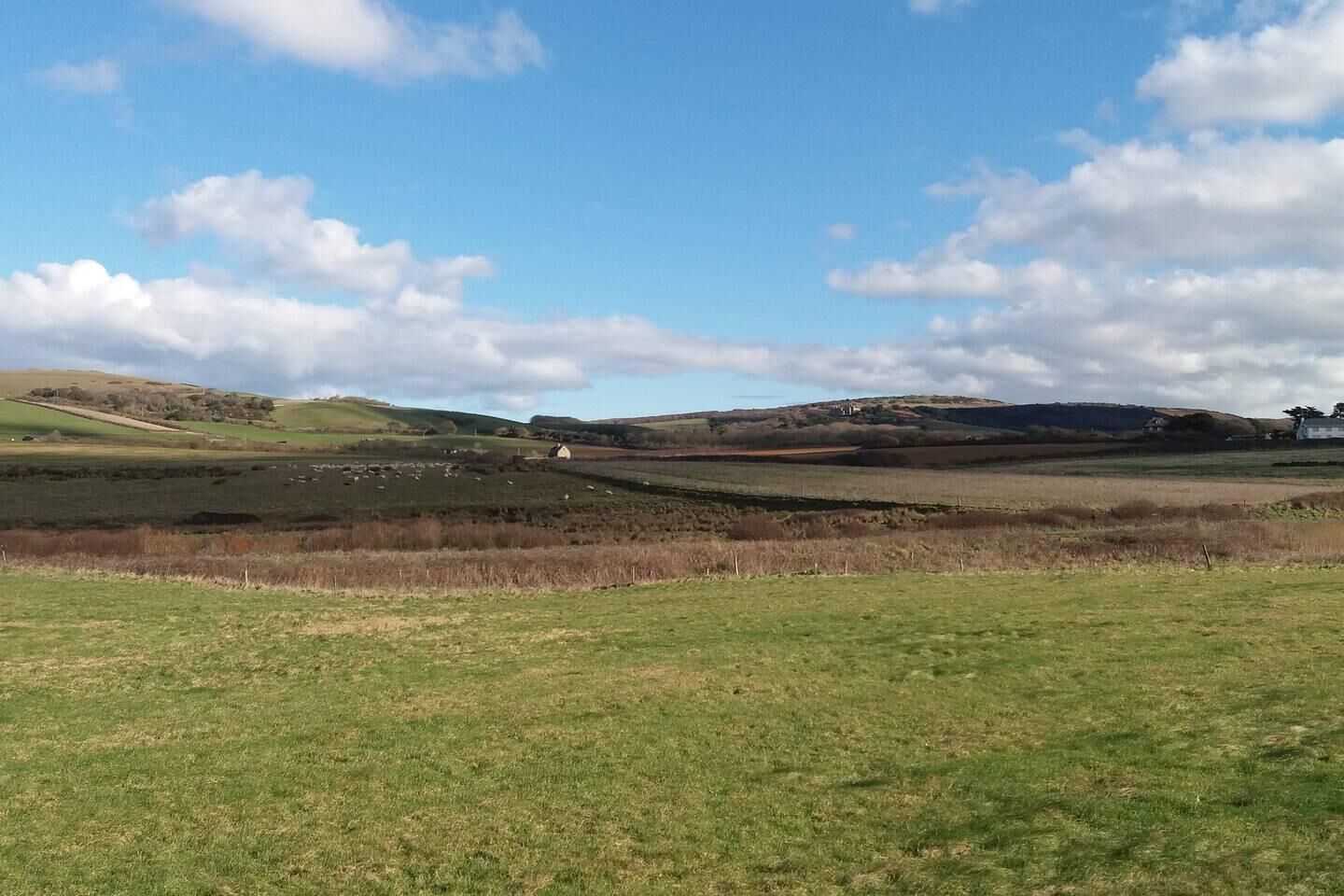 A rural landscape with rolling hills, a field, and a distant building.